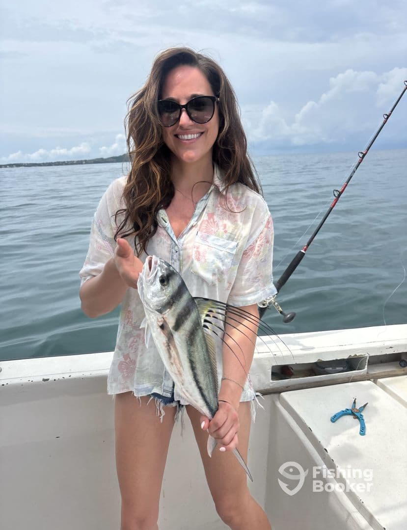 A smiling angler proudly displaying a striped fish while fishing on a boat, showcasing a beautiful day on the water.