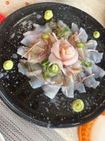 A beautifully arranged plate of sashimi featuring thinly sliced fish, garnished with herbs and sauces, showcasing culinary presentation.