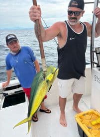 Two anglers aboard a fishing boat, with one proudly displaying a vibrant Mahi Mahi caught during their offshore adventure.