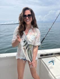 A smiling angler proudly displaying a striped fish while fishing on a boat, showcasing a beautiful day on the water.