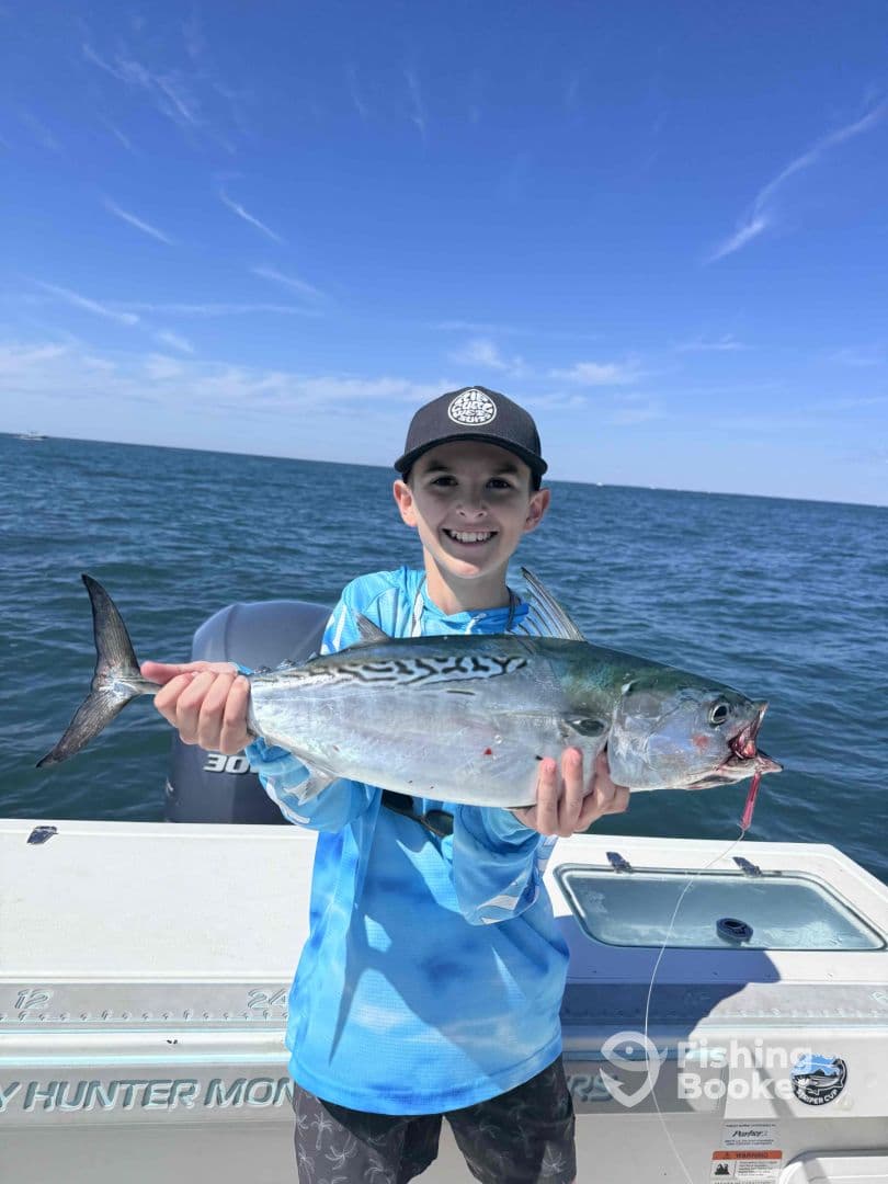 A young angler proudly displaying a large fish while on a fishing trip, with a clear blue sky and ocean in the background.