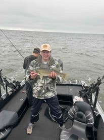 Angler proudly displaying a Walleye while fishing on a boat in a freshwater lake.