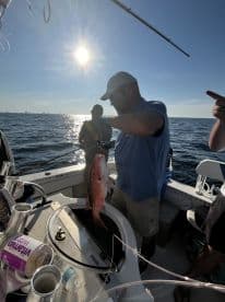 Angler reeling in a Red Snapper while fishing on a sunny day in open waters.