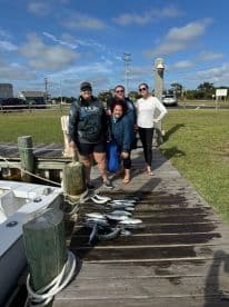 A group of four anglers proudly posing with their catch of the day, featuring several fish displayed on the dock after a successful fishing trip.