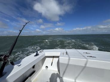 A fishing rod bent under tension as the boat navigates through choppy waters, showcasing an active fishing environment.