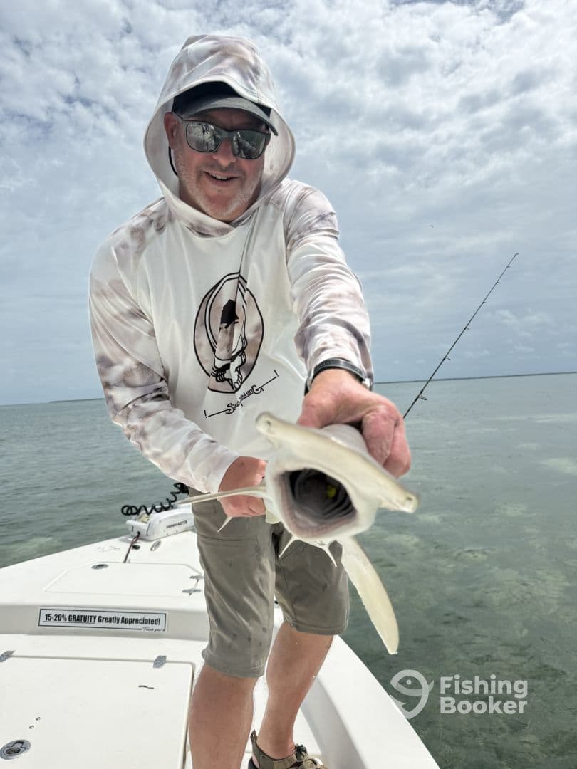 An angler proudly displaying a caught fish while standing on a boat in a clear water fishing environment.