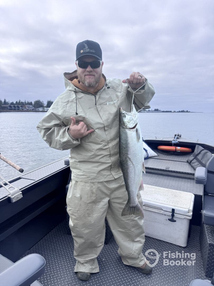 An angler proudly displaying a large Salmon while aboard a fishing boat, showcasing a successful day on the water.