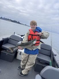 A young angler proudly displaying a caught fish while aboard a fishing boat, showcasing a scenic water backdrop.