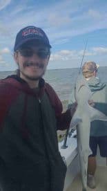 An angler proudly displaying a caught shark while fishing on a boat, with another fisherman in the background.