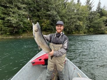 Angler proudly displaying a large Salmon while fishing from a small boat in a scenic river environment.