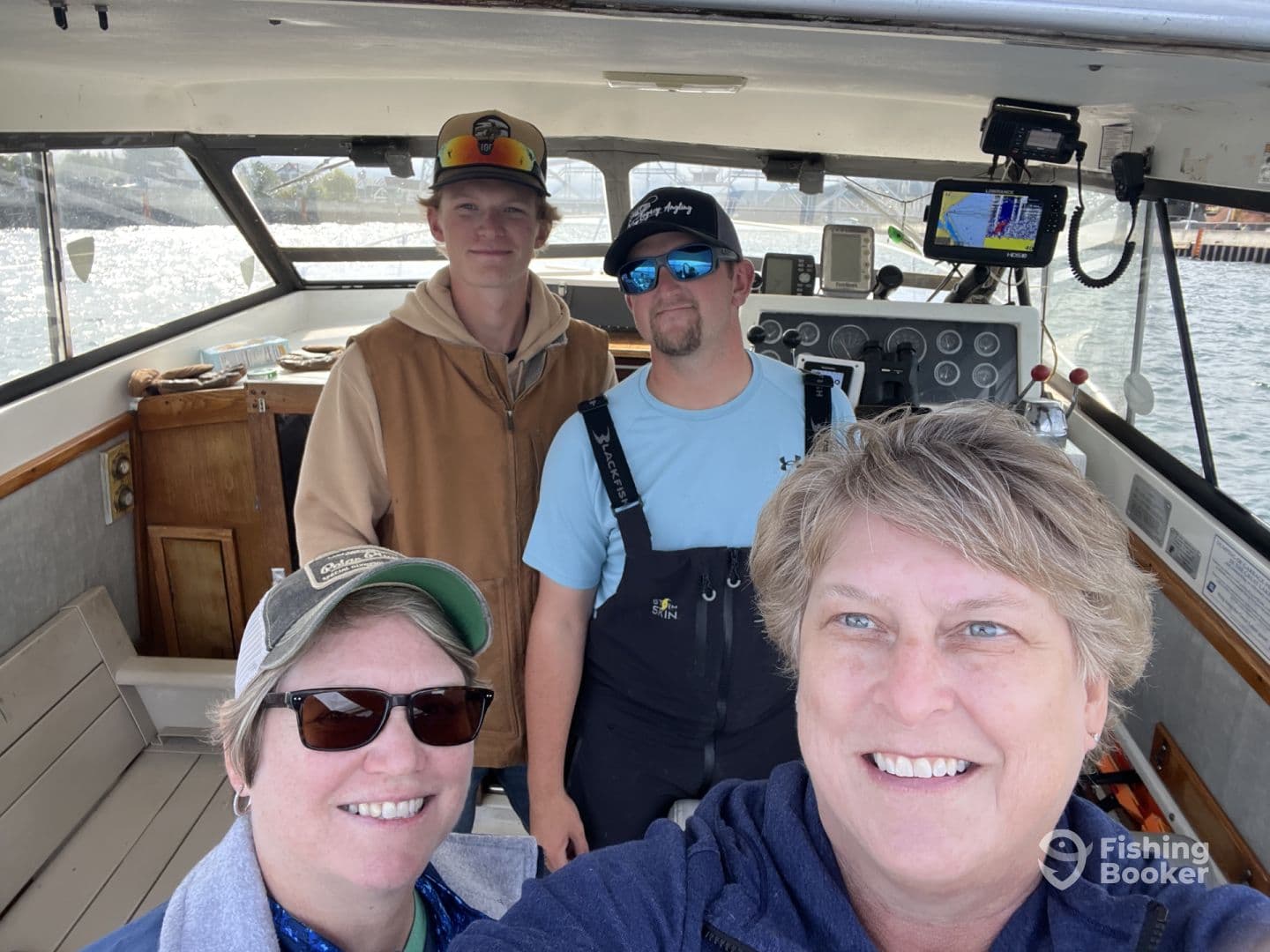 A group of four individuals inside a fishing boat, showcasing the helm and seating area, ready for a day of fishing.