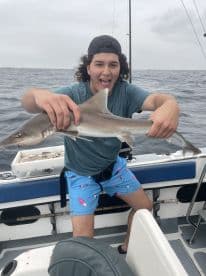 Enthusiastic angler holding a small shark while fishing offshore, showcasing a successful catch during a deep-sea adventure.