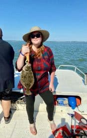 Angler proudly displaying a Flounder while fishing on a boat in a coastal waterway.