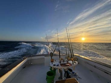 A scenic view from the interior of a fishing boat, showcasing fishing rods and a beautiful sunset over the ocean.