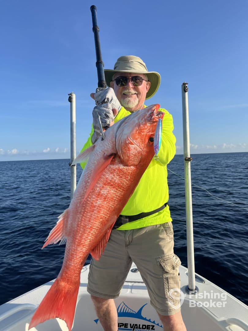An angler proudly displaying a large Red Snapper while fishing offshore, showcasing a bright sunny day and clear blue waters.
