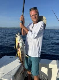 An angler proudly displaying a large Yellowfin Tuna while fishing offshore, showcasing the excitement of a successful catch.