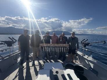 A group of anglers proudly displaying their catch of the day on a fishing charter in Lake Tahoe, with several fish arranged on a board and the scenic backdrop of mountains and water.