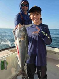 A young angler proudly displays a large fish while fishing on a boat, showcasing a successful day on the water.