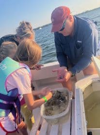 A group of young anglers, including children, are engaged in catching shrimp on a boat, showcasing a hands-on fishing experience in a scenic waterway.