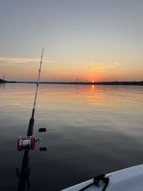 A serene sunset view over calm waters with a fishing rod in the foreground, showcasing a peaceful fishing environment.