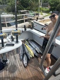 An angler proudly displaying a variety of fish, including a large Mahi Mahi, on the deck of a fishing boat after a successful outing.