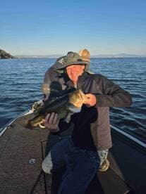 An angler proudly displaying a large Largemouth Bass while fishing from a Vexus boat on a clear day.