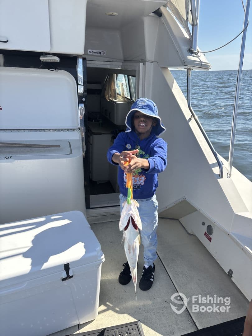 A young angler proudly displaying a catch of two fish while aboard a fishing boat, enjoying a day on the water.