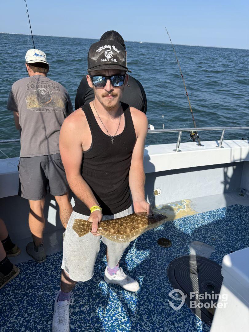 Angler proudly displaying a Flounder while fishing on a boat, showcasing a sunny day on the water.