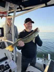 An angler proudly displaying a Walleye caught while fishing on a boat, with another person in the background enjoying the moment.