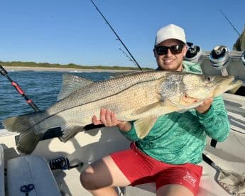 An angler proudly displaying a large Snook while fishing on a boat, showcasing a beautiful day on the water.