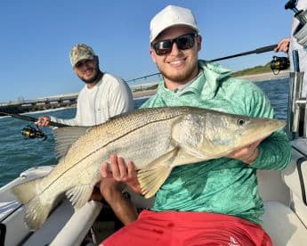 Two anglers aboard a boat, with one proudly displaying a large Snook caught during a fishing trip.