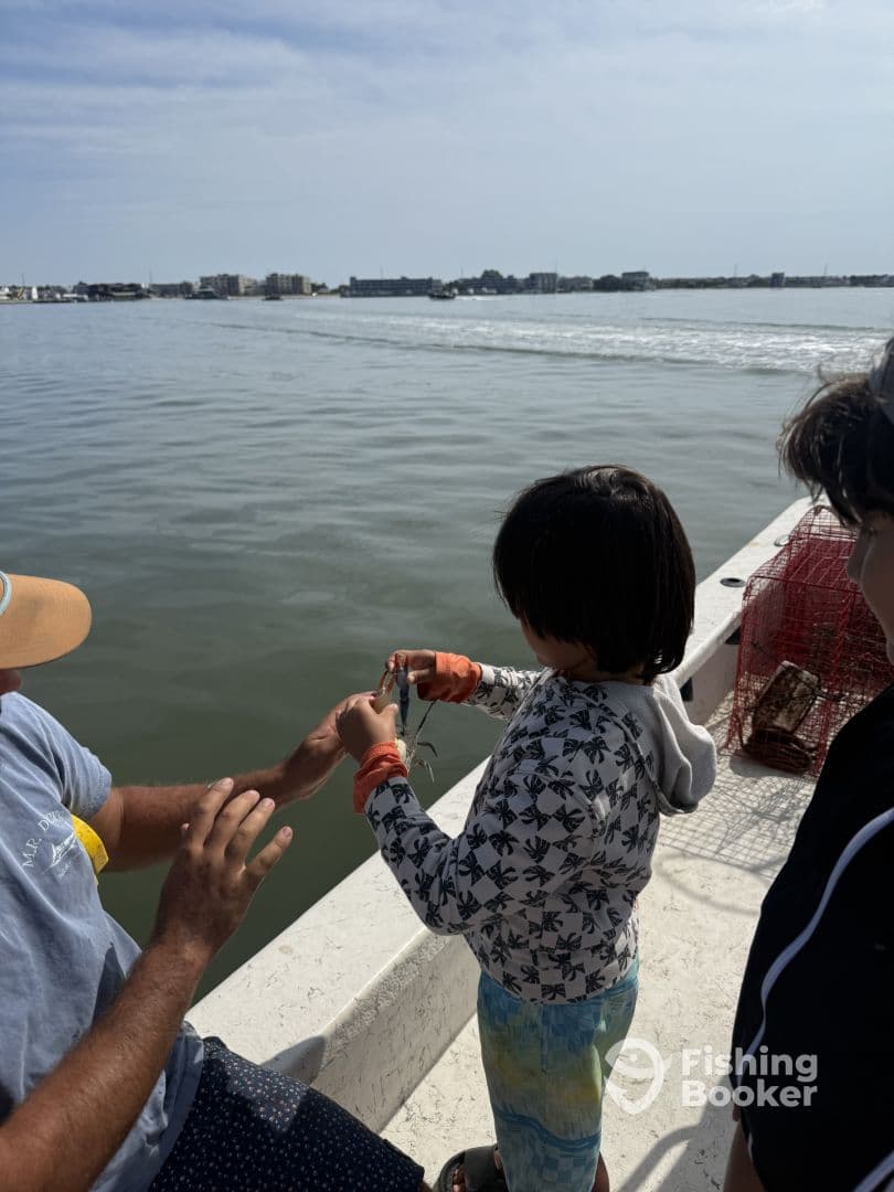 A young angler learning to handle a fish while fishing from a boat, with a scenic waterfront in the background.