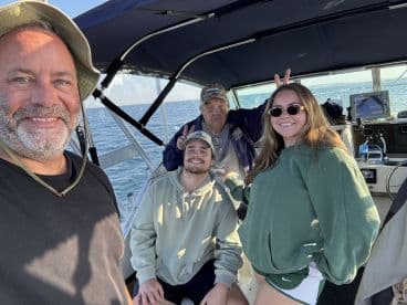 A cheerful group of four enjoying a fishing trip aboard a boat, showcasing the interior seating and a sunny day on the water.