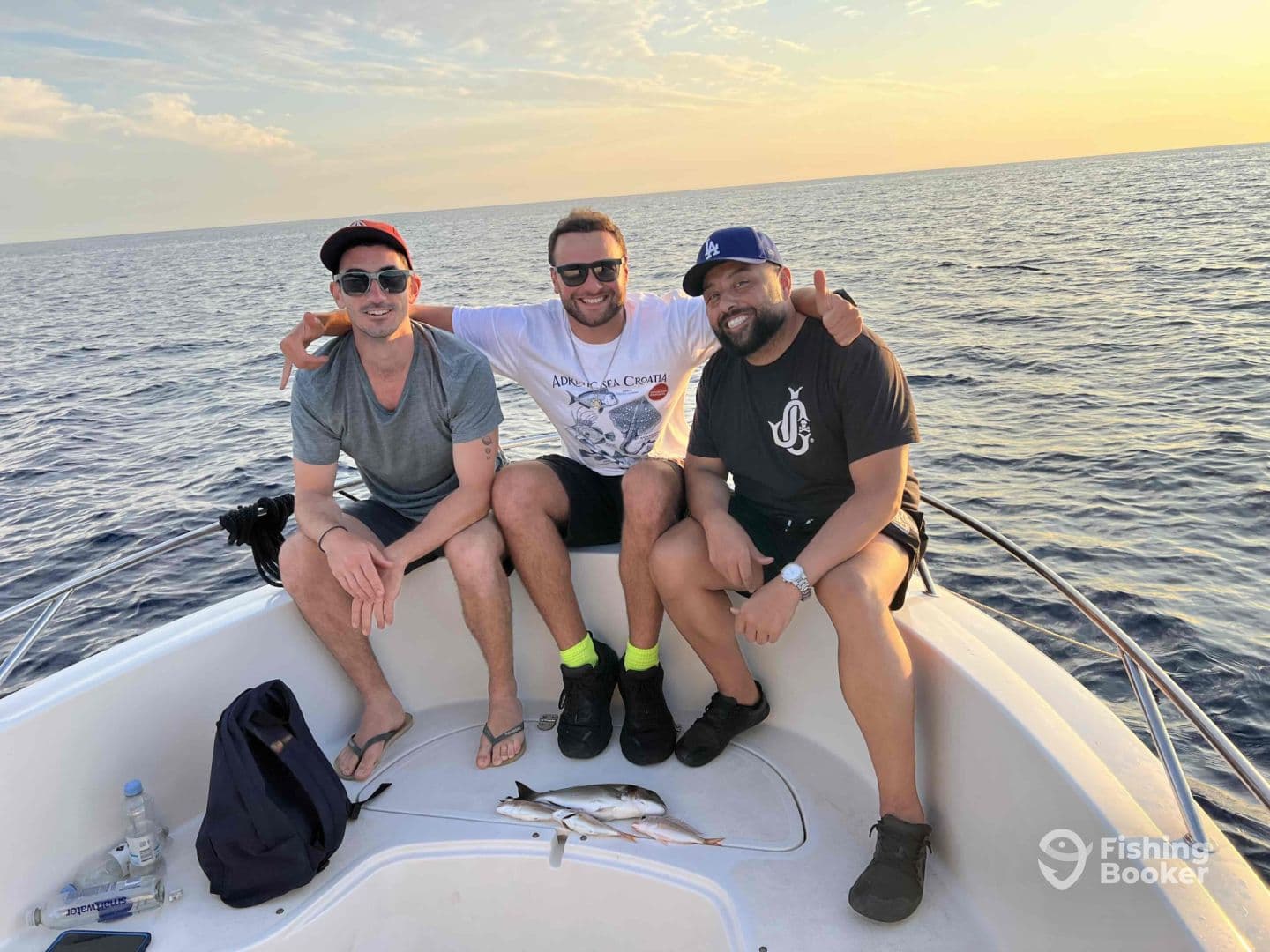 Three friends enjoying a sunset fishing trip on a boat, showcasing their catch of small fish in the background.