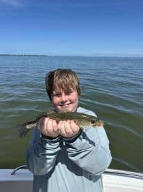 A young angler proudly displaying a Speckled Trout while fishing on a sunny day.