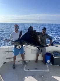 Two anglers proudly displaying a large Sailfish aboard a sportfishing boat in open waters.