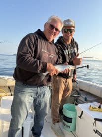Two anglers proudly displaying a caught fish aboard a fishing boat, enjoying a day on the water.