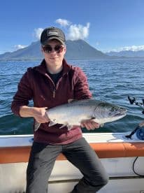 A young angler proudly displaying a freshly caught Salmon while enjoying a scenic day on the water.