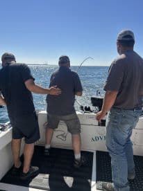 Three anglers actively reeling in a catch while enjoying a sunny day on the open water.