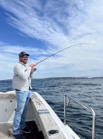Angler actively reeling in a fish while enjoying a sunny day on the water, with a city skyline visible in the background.