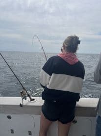 A young angler is actively reeling in a fish while fishing on a boat, showcasing the excitement of the catch in open waters.