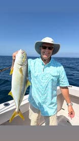 An angler proudly displaying a Yellowtail Snapper while fishing on a sunny day in open waters.
