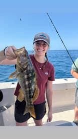 A young woman proudly displaying her catch, a large fish, while fishing on a boat in open waters.