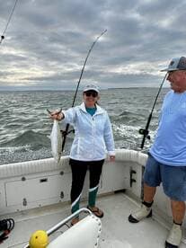 An angler proudly displaying a Speckled Trout while fishing on a boat, showcasing a cloudy day on the water.