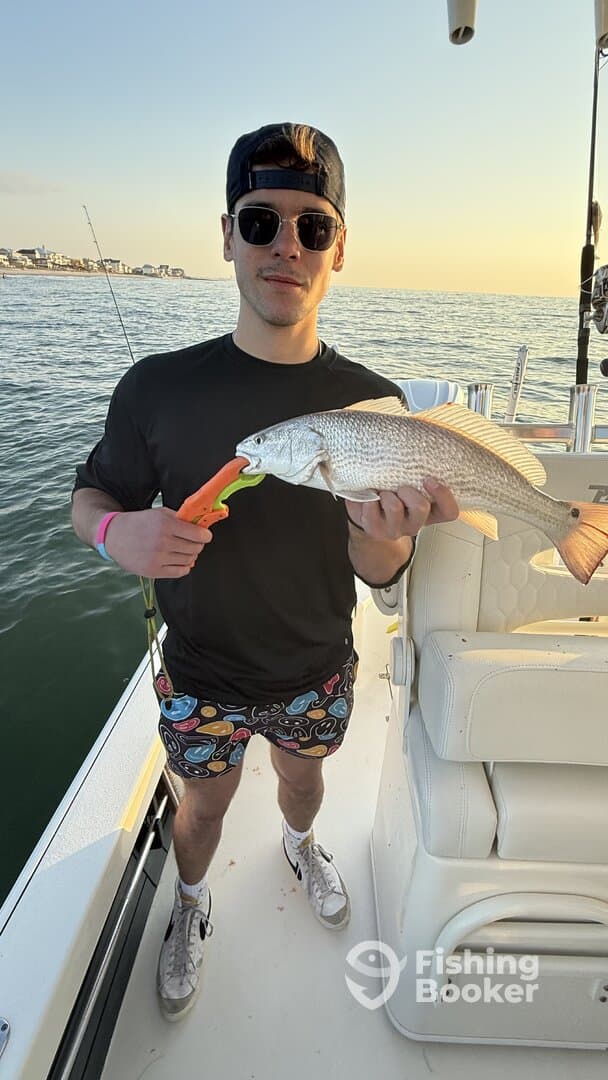 An angler proudly displaying a Redfish while fishing on a boat during sunset.