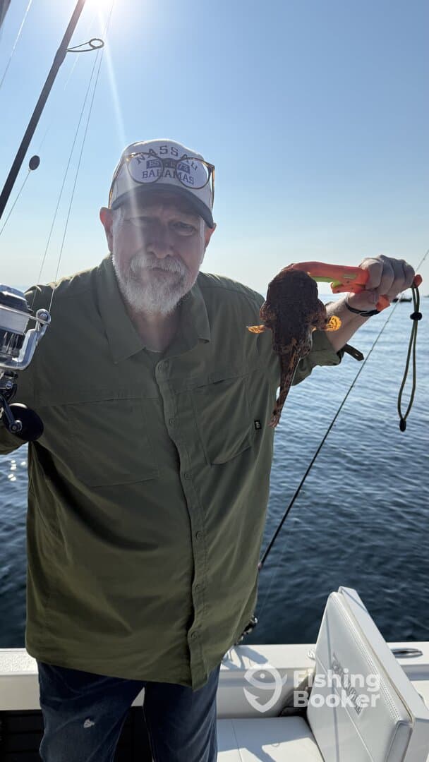An angler proudly displaying a large octopus caught while fishing on a boat, with calm waters in the background.