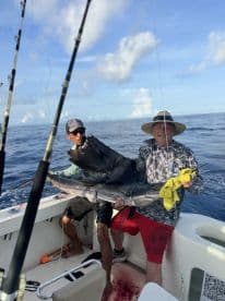 Two anglers proudly displaying a large Sailfish aboard a fishing boat in open waters.