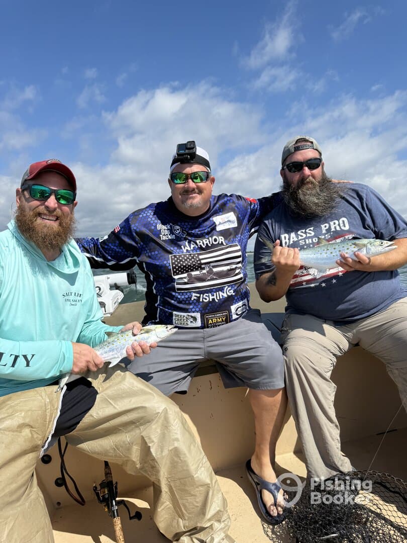 Three anglers proudly displaying their catches aboard a fishing boat, showcasing a sunny day on the water.