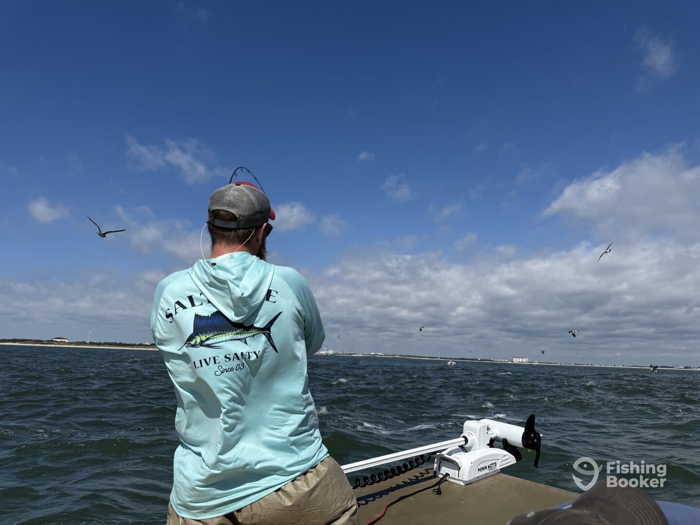 Angler casting a line while fishing in a coastal environment, with birds flying overhead and a scenic backdrop.