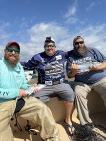 Three anglers proudly displaying their catches aboard a fishing boat, showcasing a sunny day on the water.